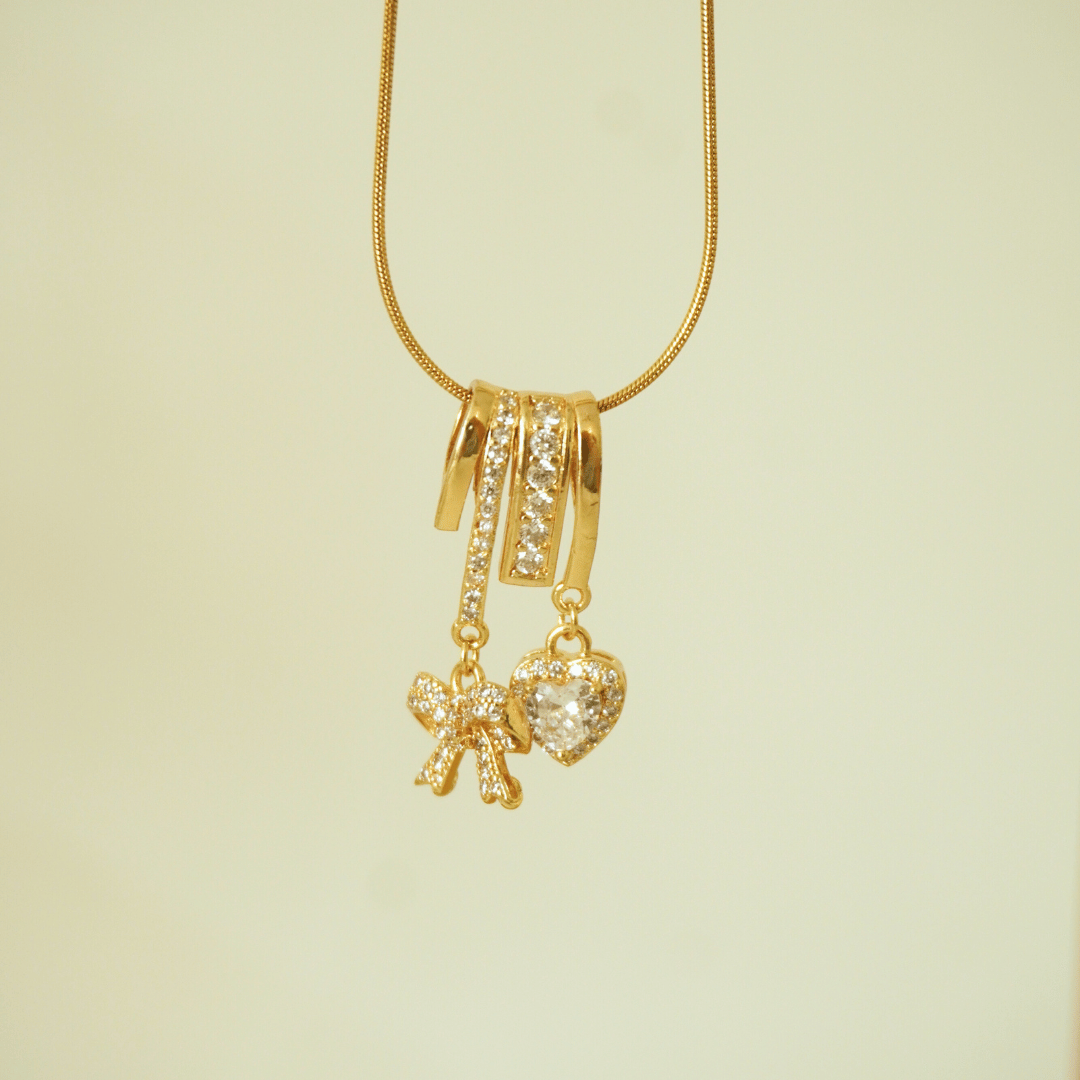 Gold necklace with heart and bow-shaped charms on a light green background
